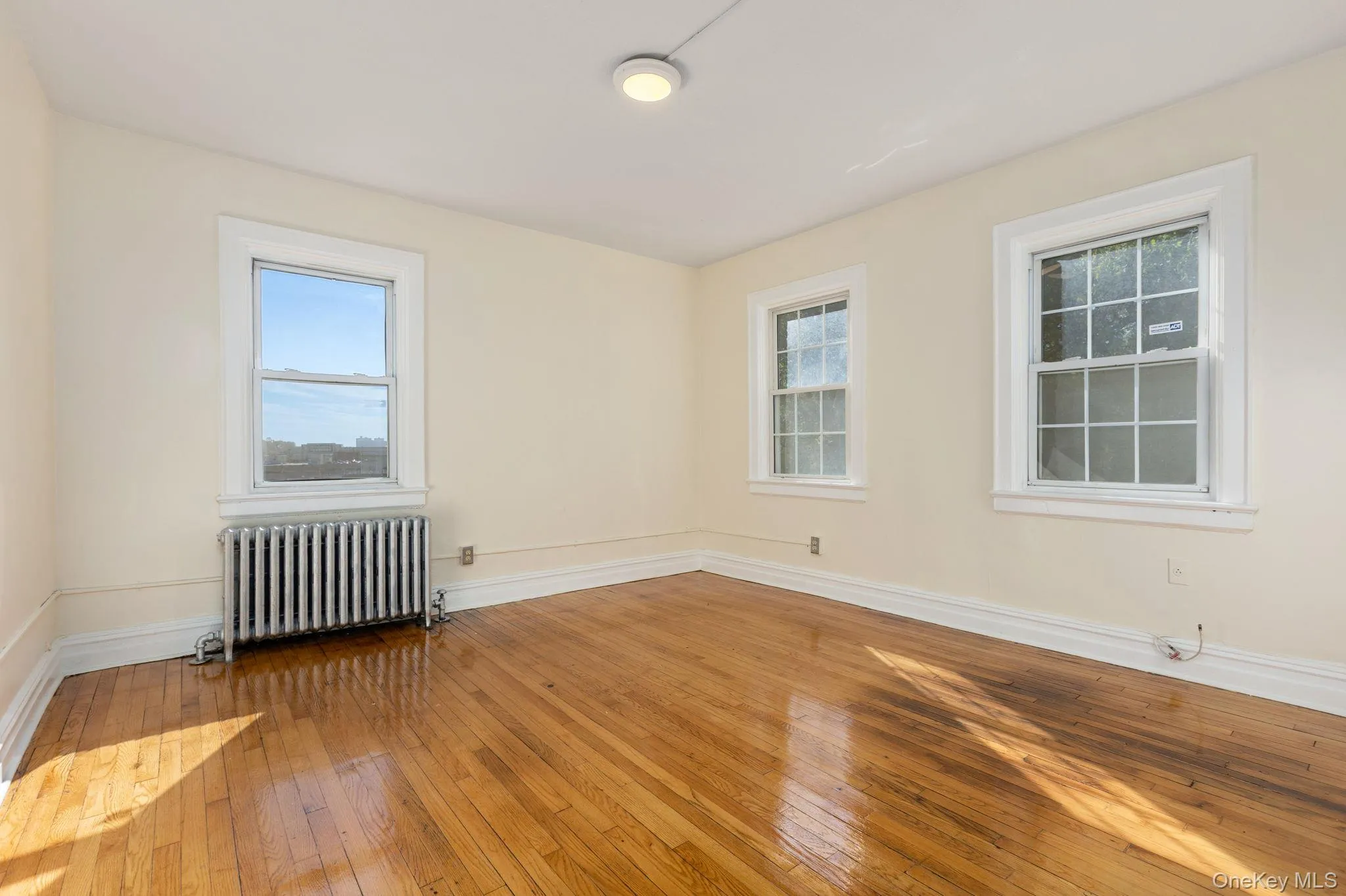 Empty room with hardwood / wood-style floors, healthy amount of natural light, and radiator heating unit Empty room with hardwood / wood-style floors, healthy amount of natural light, and radiator heating unit
