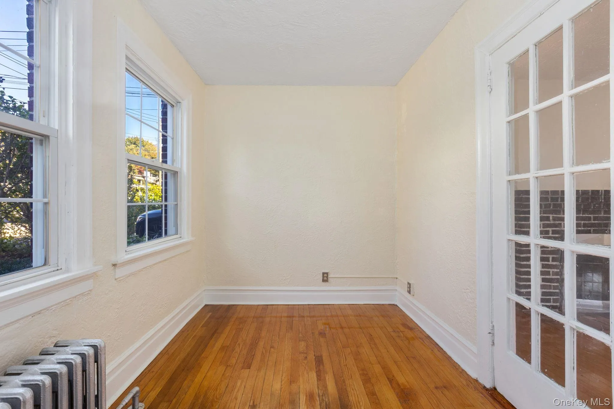 Empty room with hardwood / wood-style floors, radiator heating unit, and a textured wall Empty room with hardwood / wood-style floors, radiator heating unit, and a textured wall