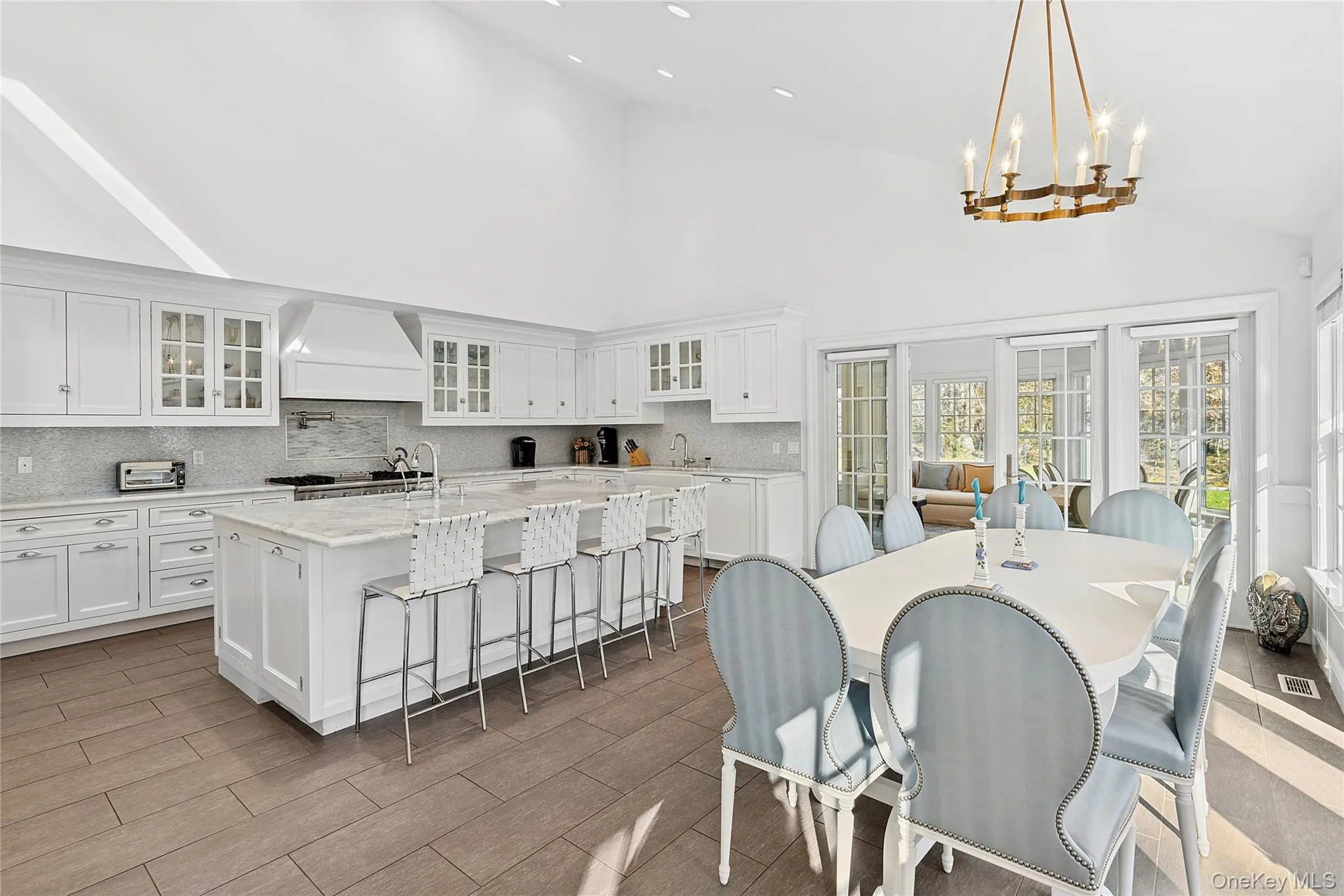 Kitchen featuring glass insert cabinets, high vaulted ceiling, white cabinetry, a kitchen bar, and light stone countertops