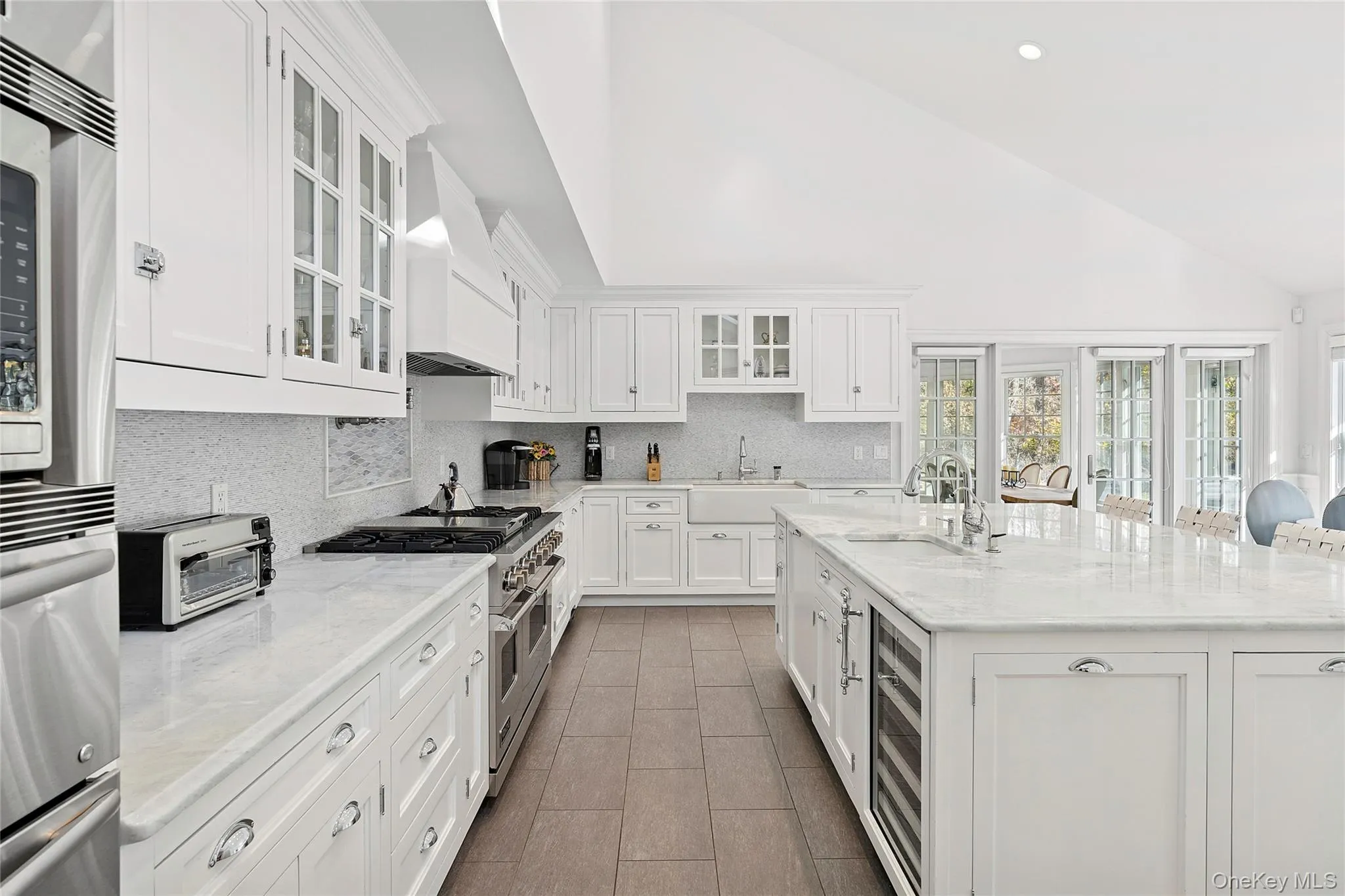 Kitchen featuring white cabinetry, glass insert cabinets, stainless steel appliances, light stone countertops, and high vaulted ceiling