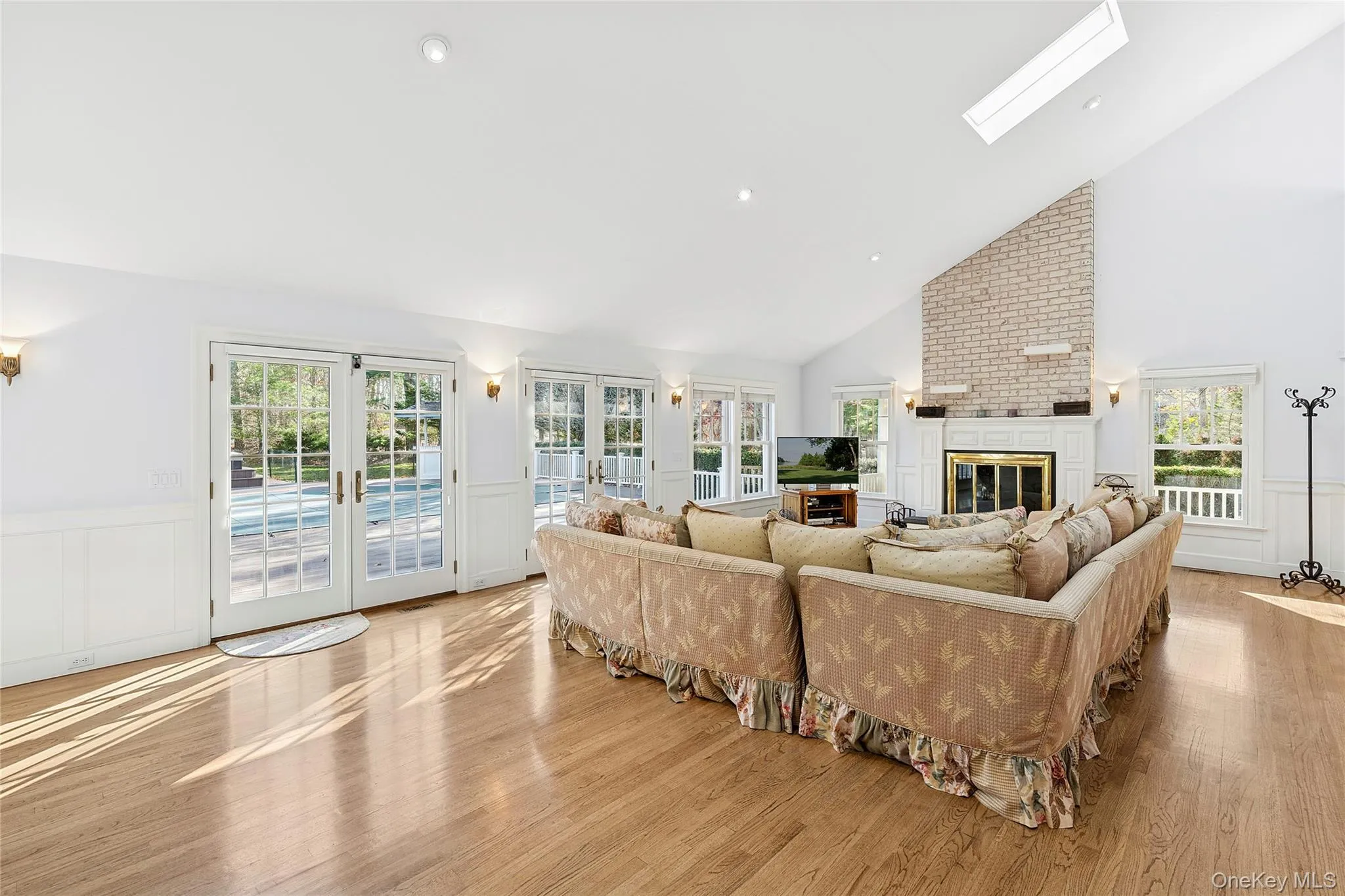 Living area with a decorative wall, wainscoting, high vaulted ceiling, french doors, and light wood-style floors