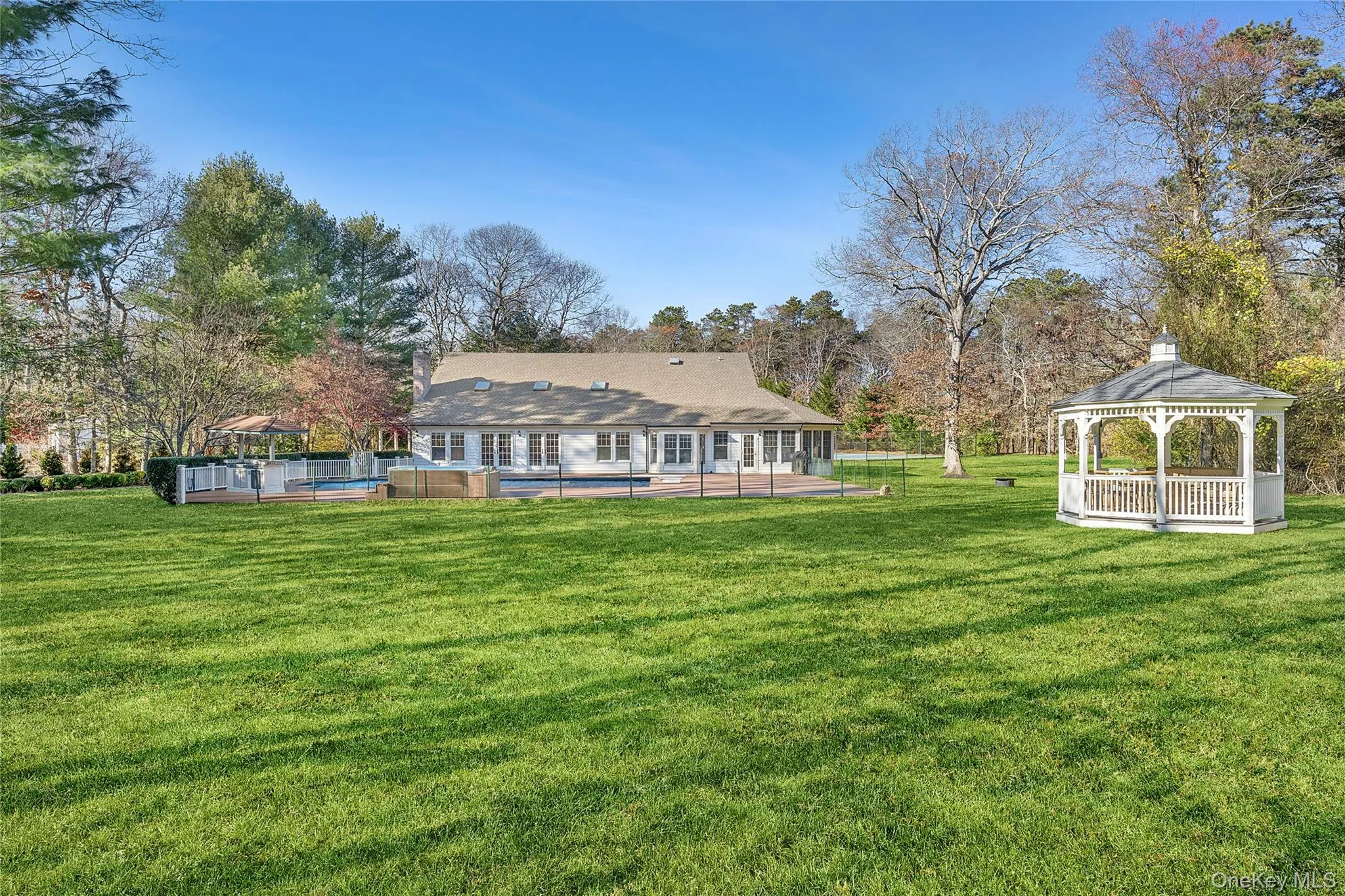 Back of property featuring an outdoor pool, a lawn, a gazebo, and view of wooded area