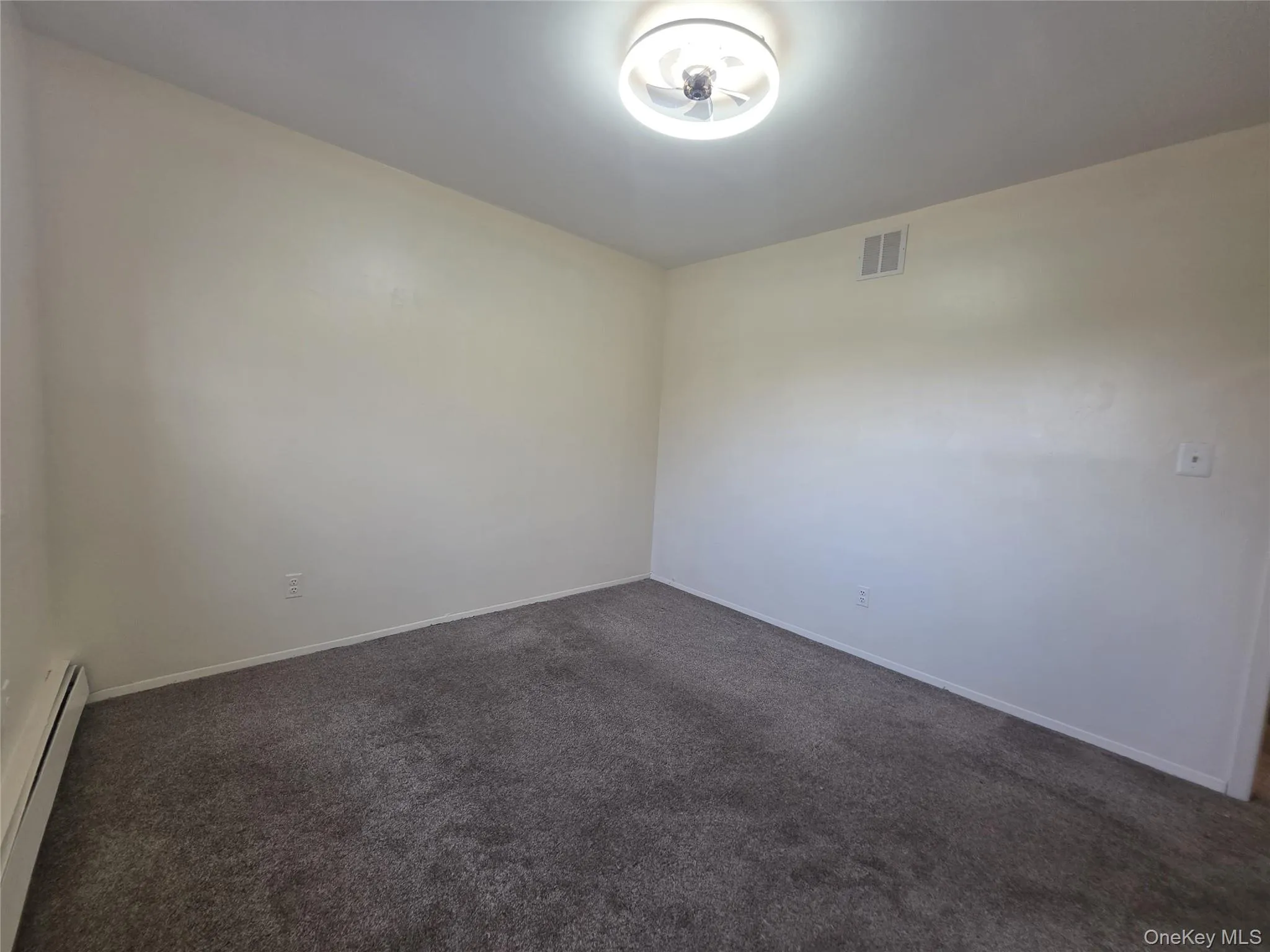 Empty room featuring dark colored carpet and a baseboard heating unit Empty room featuring dark colored carpet and a baseboard heating unit