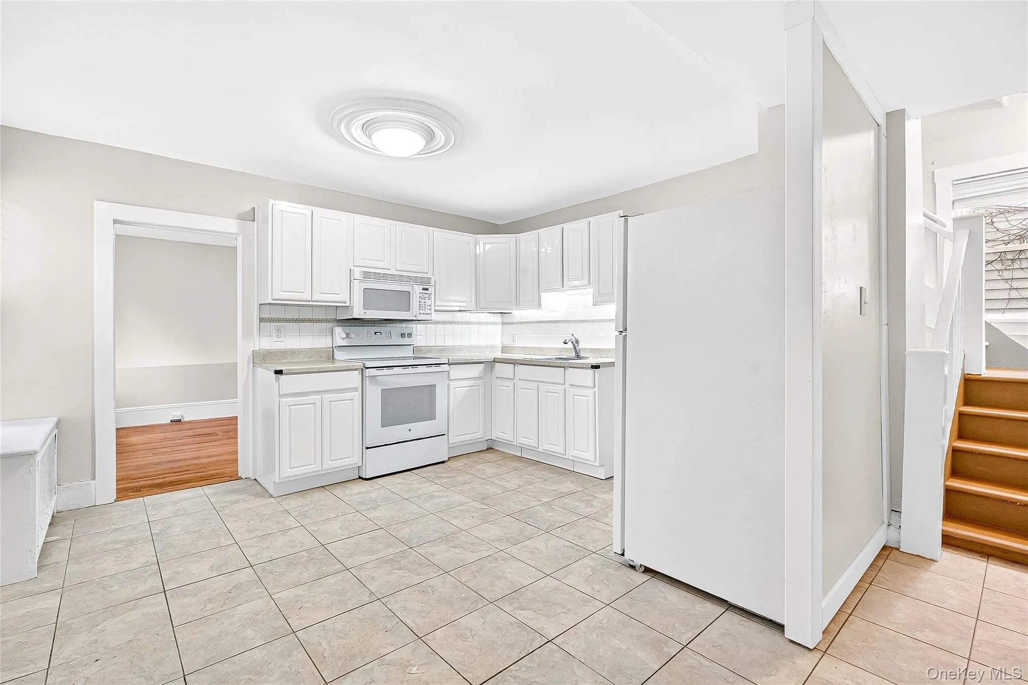 Kitchen featuring white appliances, backsplash, white cabinets, light tile patterned flooring, and light countertops Kitchen featuring white appliances, backsplash, white cabinets, light tile patterned flooring, and light countertops