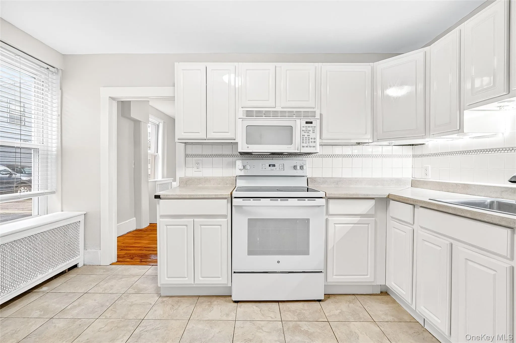 Kitchen with white appliances, light countertops, radiator, and tasteful backsplash Kitchen with white appliances, light countertops, radiator, and tasteful backsplash