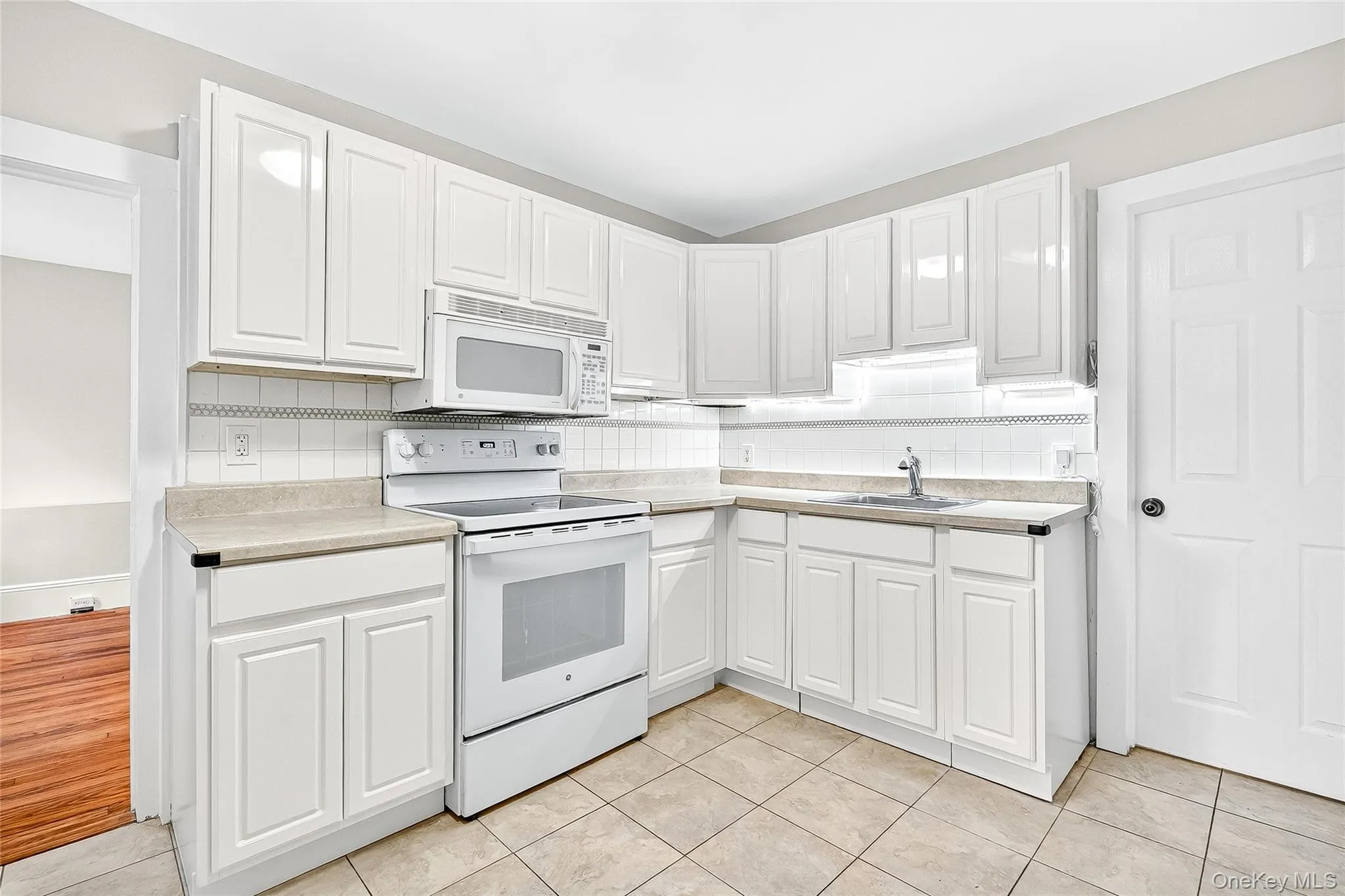 Kitchen featuring white appliances, backsplash, and white cabinetry Kitchen featuring white appliances, backsplash, and white cabinetry