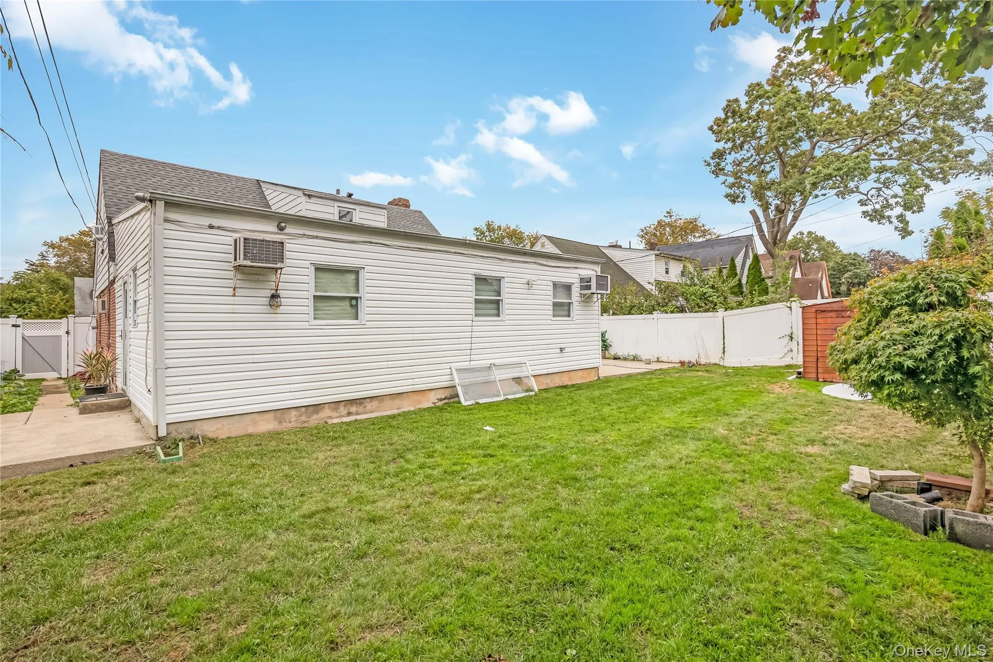 Rear view of house featuring a gate, a fenced backyard, a wall mounted AC, roof with shingles, and a patio area Rear view of house featuring a gate, a fenced backyard, a wall mounted AC, roof with shingles, and a patio area