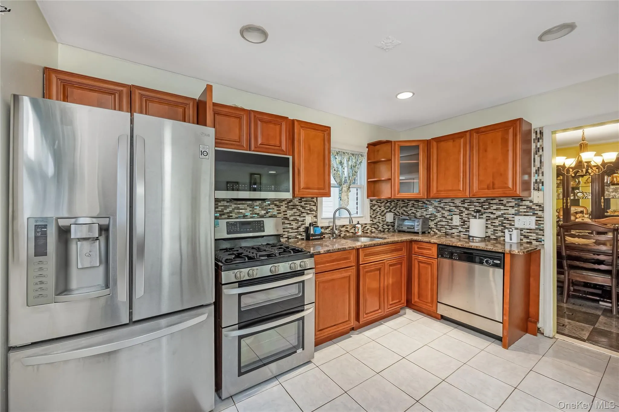 Kitchen featuring appliances with stainless steel finishes, brown cabinets, light tile patterned floors, decorative backsplash, and recessed lighting Kitchen featuring appliances with stainless steel finishes, brown cabinets, light tile patterned floors, decorative backsplash, and recessed lighting