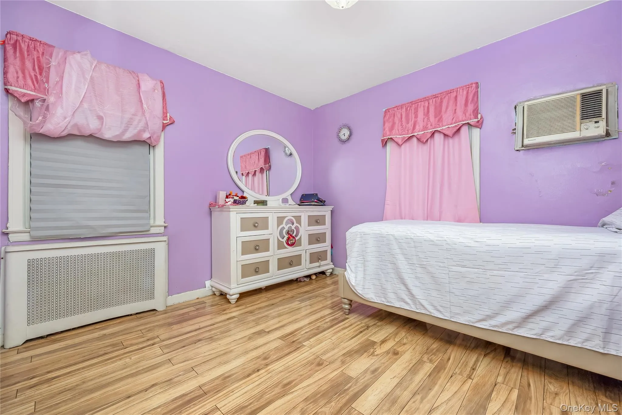 Bedroom with radiator heating unit, wood finished floors, and a wall unit AC Bedroom with radiator heating unit, wood finished floors, and a wall unit AC