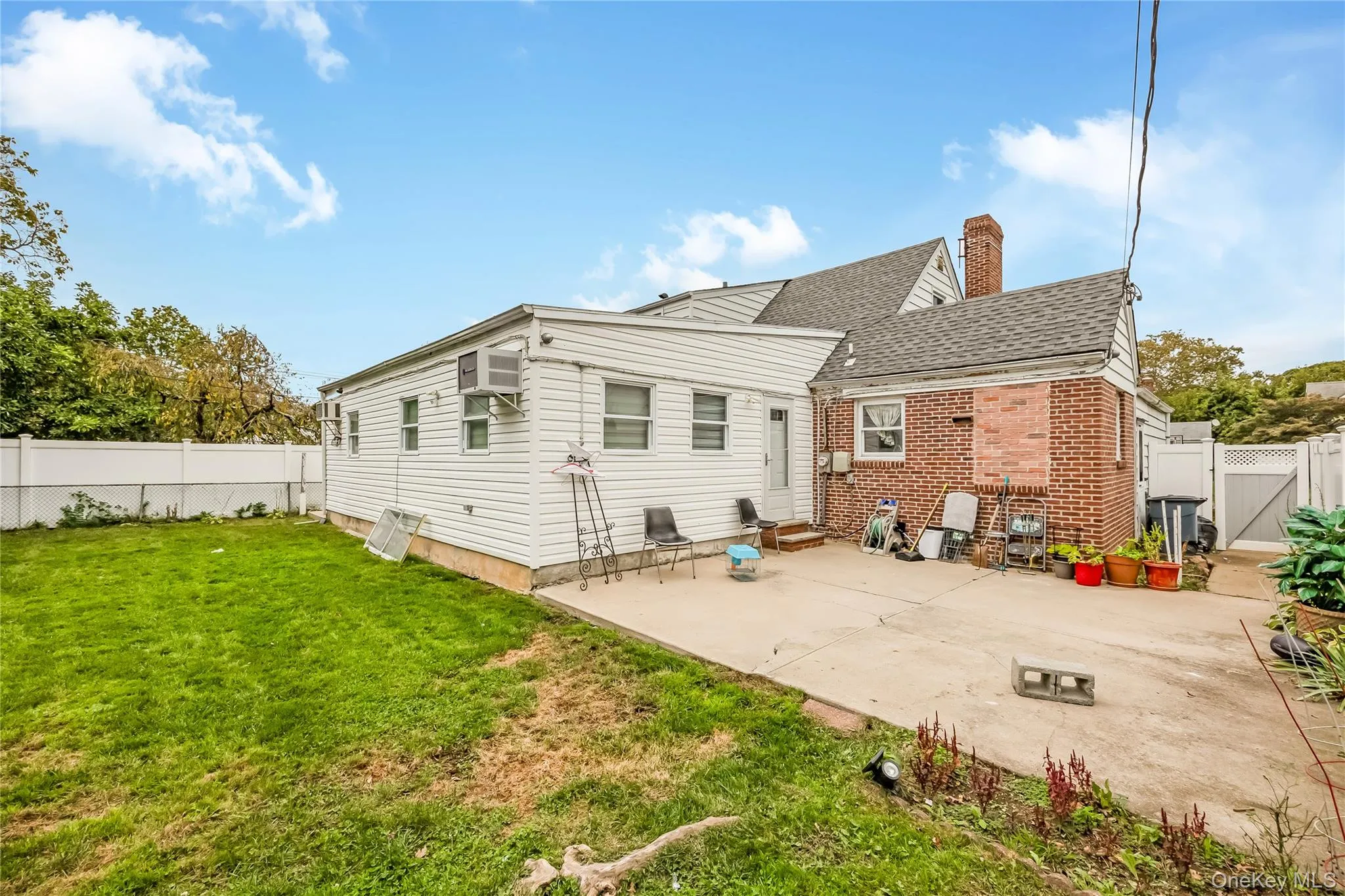 Rear view of house with a fenced backyard, a gate, a patio, a chimney, and brick siding Rear view of house with a fenced backyard, a gate, a patio, a chimney, and brick siding