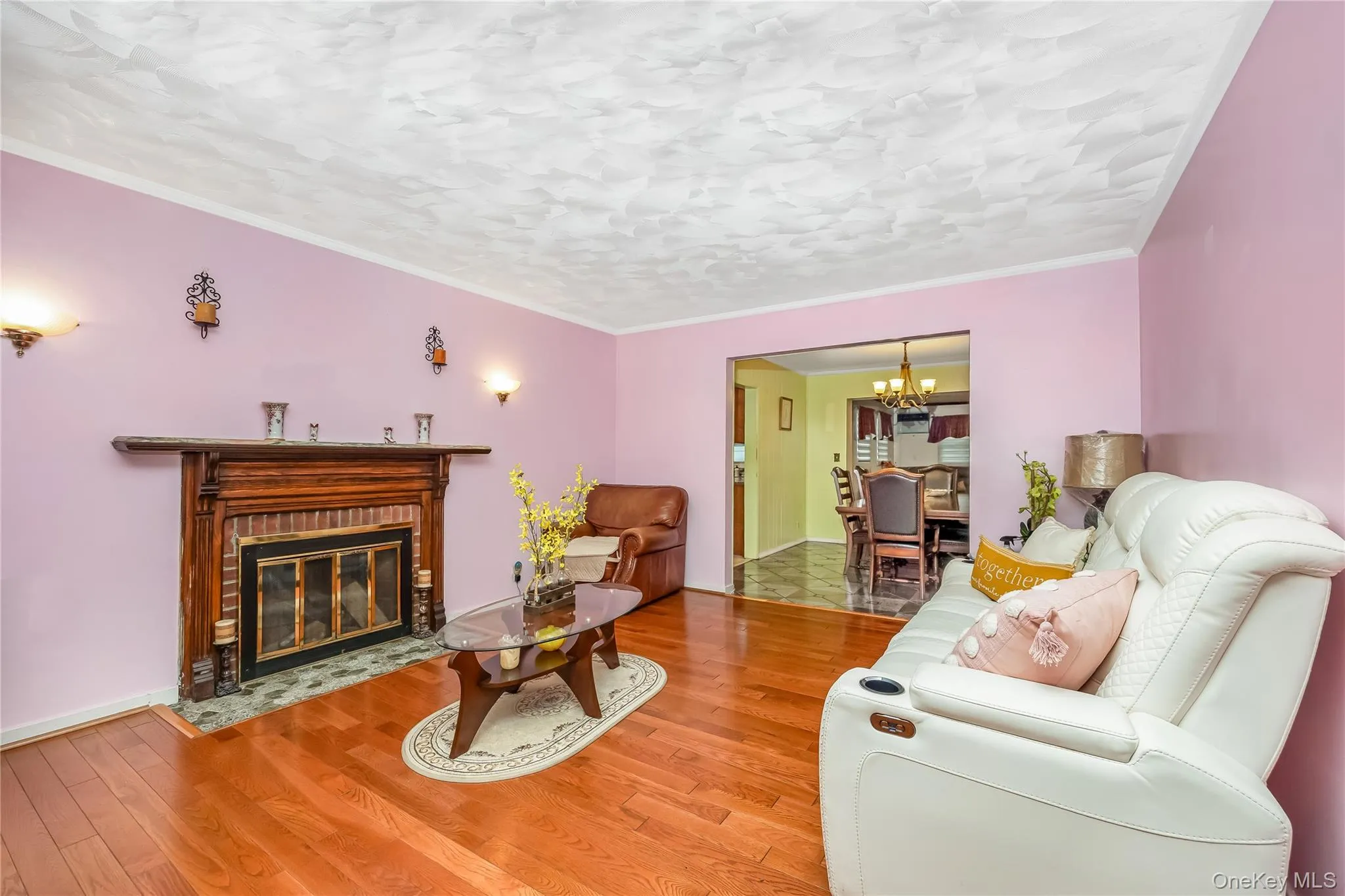 Living room featuring wood finished floors, a fireplace with flush hearth, a chandelier, and crown molding Living room featuring wood finished floors, a fireplace with flush hearth, a chandelier, and crown molding