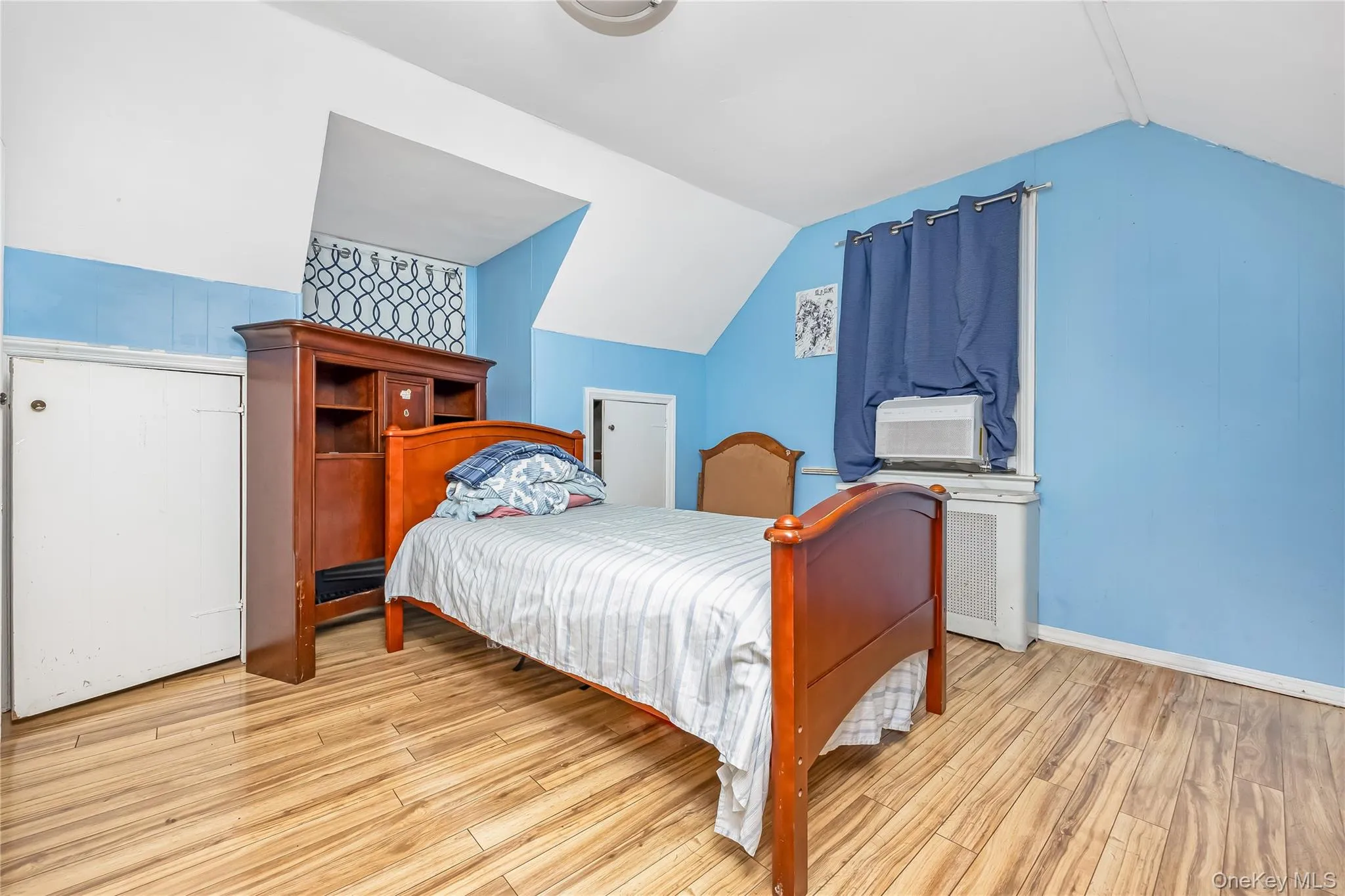 Bedroom featuring vaulted ceiling, light wood-type flooring, and radiator heating unit Bedroom featuring vaulted ceiling, light wood-type flooring, and radiator heating unit