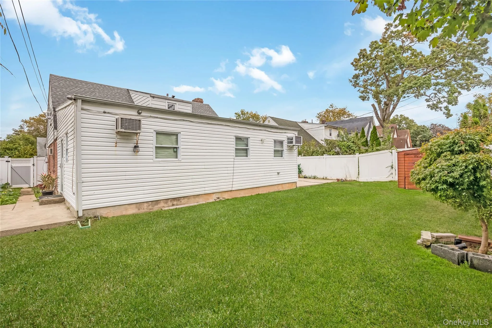 Rear view of house with a fenced backyard, a gate, a wall mounted AC, a shingled roof, and a patio Rear view of house with a fenced backyard, a gate, a wall mounted AC, a shingled roof, and a patio