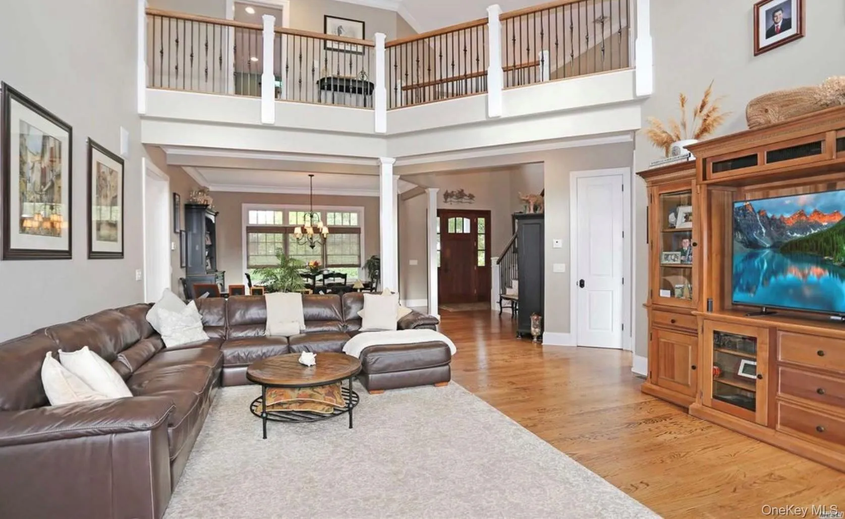 Living room featuring a high ceiling, light wood-style floors, crown molding, a chandelier, and stairway Living room featuring a high ceiling, light wood-style floors, crown molding, a chandelier, and stairway