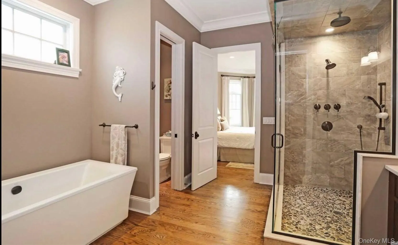 Ensuite bathroom with a stall shower, light wood finished floors, a soaking tub, and ornamental molding Ensuite bathroom with a stall shower, light wood finished floors, a soaking tub, and ornamental molding