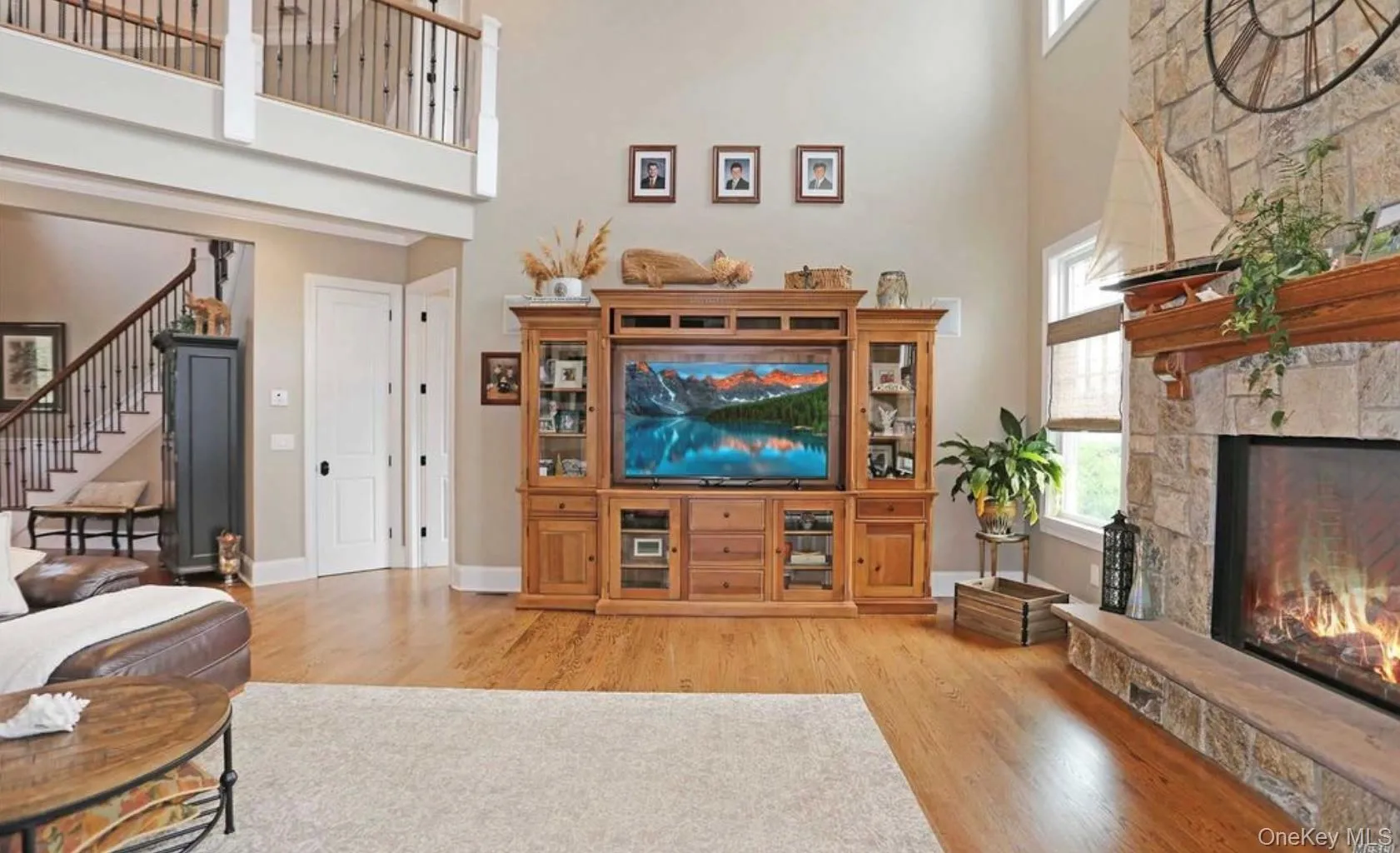 Living room featuring a high ceiling, light wood-type flooring, a stone fireplace, and stairway Living room featuring a high ceiling, light wood-type flooring, a stone fireplace, and stairway