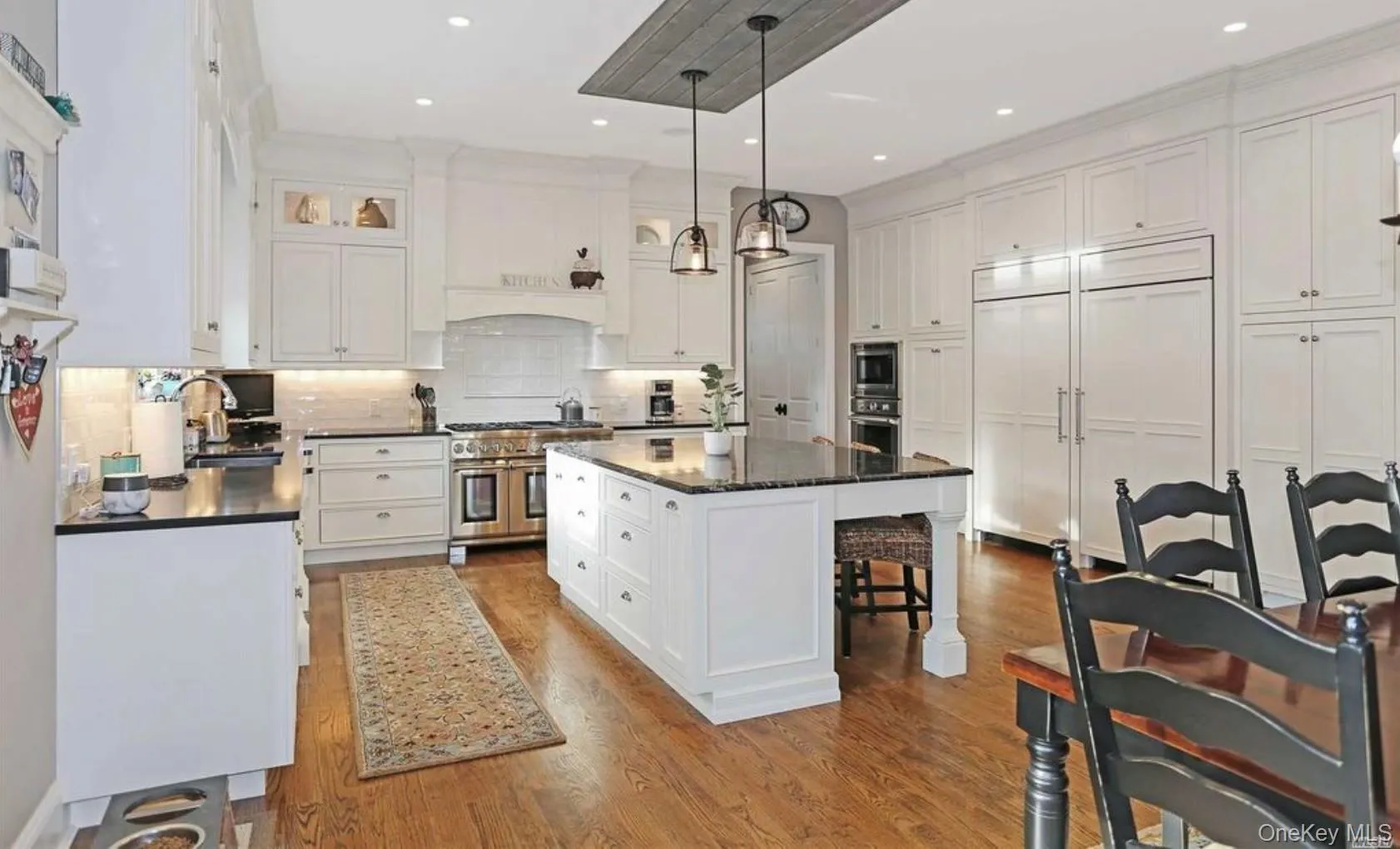 Kitchen featuring backsplash, hanging light fixtures, white cabinetry, dark wood-type flooring, and built in appliances Kitchen featuring backsplash, hanging light fixtures, white cabinetry, dark wood-type flooring, and built in appliances
