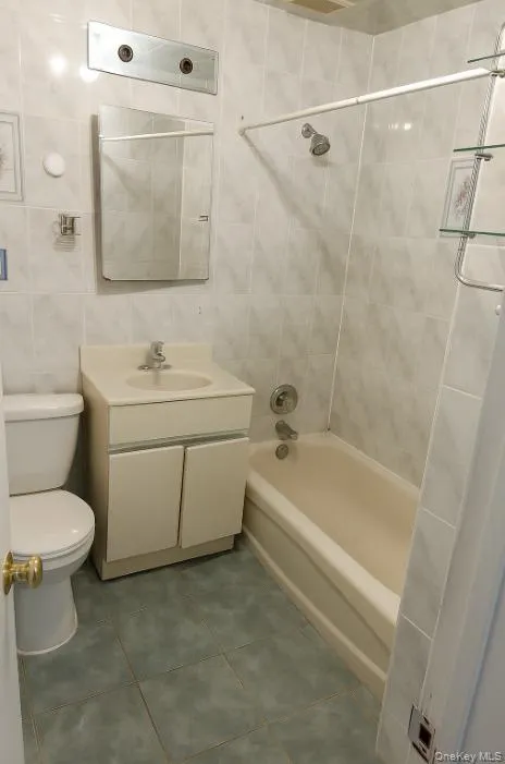 Full bathroom with tile walls, vanity, washtub / shower combination, and dark tile patterned floors Full bathroom with tile walls, vanity, washtub / shower combination, and dark tile patterned floors