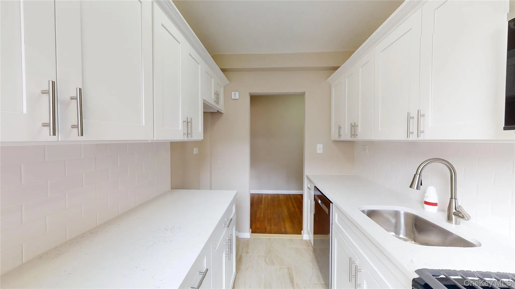 Kitchen with backsplash, white cabinetry, light stone counters, dishwasher, and light tile patterned floors Kitchen with backsplash, white cabinetry, light stone counters, dishwasher, and light tile patterned floors
