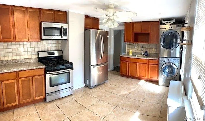 Kitchen featuring brown cabinets, stainless steel appliances, decorative backsplash, and light tile patterned flooring Kitchen featuring brown cabinets, stainless steel appliances, decorative backsplash, and light tile patterned flooring