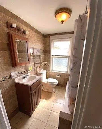 Bathroom featuring tile walls, vanity, light tile patterned floors, and a shower with curtain Bathroom featuring tile walls, vanity, light tile patterned floors, and a shower with curtain