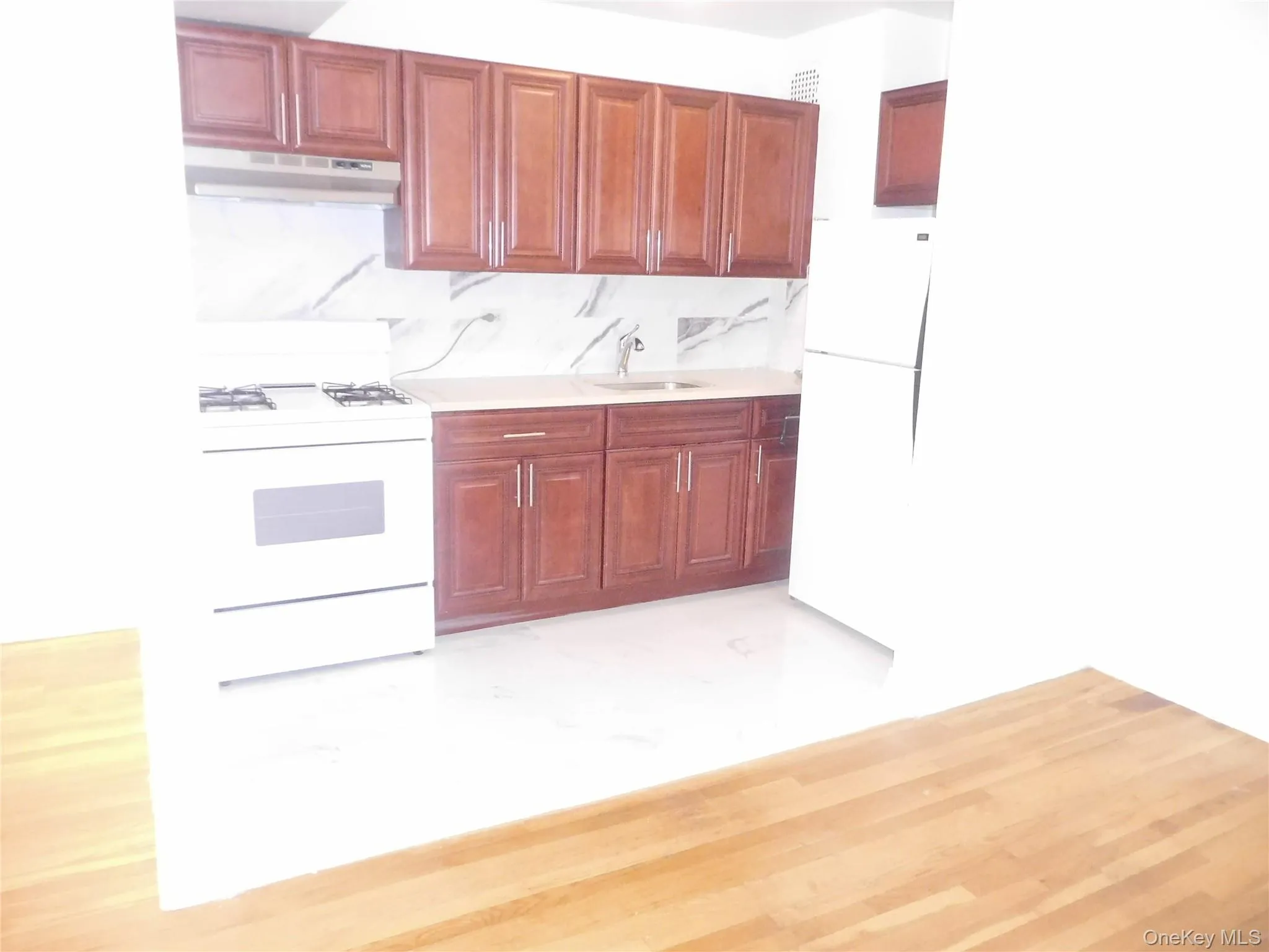 Kitchen featuring white appliances, under cabinet range hood, light wood-style floors, decorative backsplash, and reddish brown cabinets Kitchen featuring white appliances, under cabinet range hood, light wood-style floors, decorative backsplash, and reddish brown cabinets