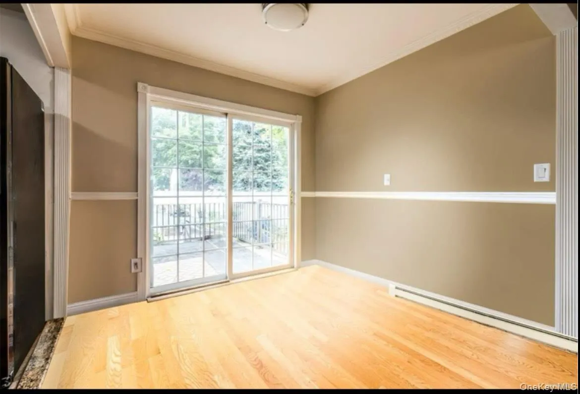 Empty room featuring a baseboard heating unit, crown molding, and wood finished floors Empty room featuring a baseboard heating unit, crown molding, and wood finished floors