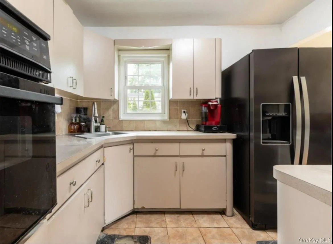 Kitchen featuring black appliances, light countertops, light tile patterned floors, and decorative backsplash Kitchen featuring black appliances, light countertops, light tile patterned floors, and decorative backsplash