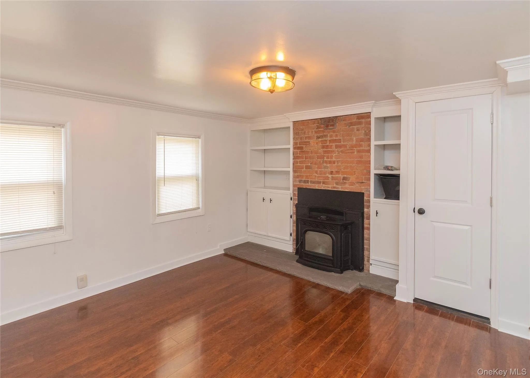 Unfurnished living room featuring dark wood-style flooring, ornamental molding, built in features, and a fireplace Unfurnished living room featuring dark wood-style flooring, ornamental molding, built in features, and a fireplace