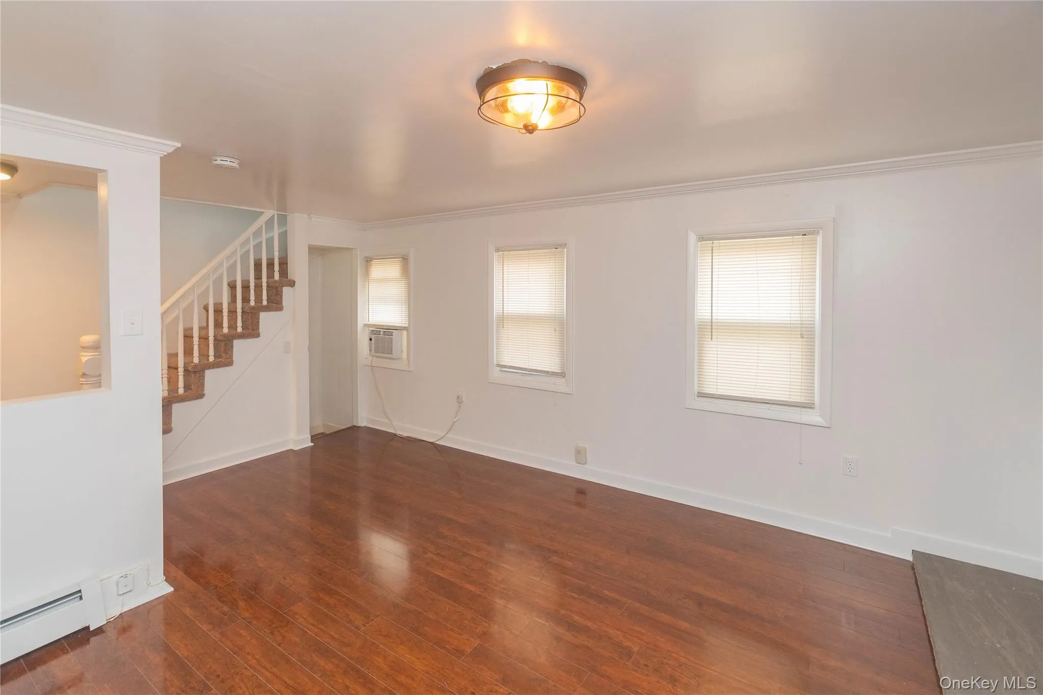 Unfurnished room featuring ornamental molding, stairs, dark wood-style floors, a baseboard heating unit, and cooling unit Unfurnished room featuring ornamental molding, stairs, dark wood-style floors, a baseboard heating unit, and cooling unit