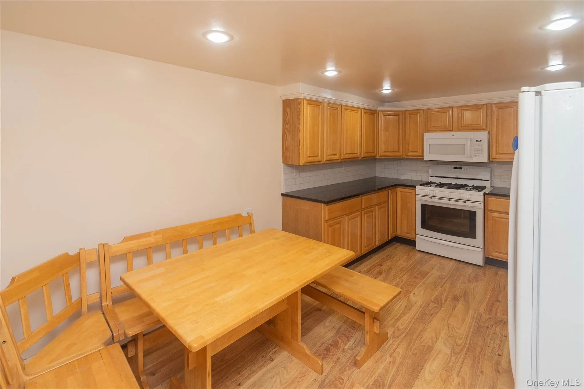 Kitchen featuring dark countertops, white appliances, light wood-style flooring, decorative backsplash, and recessed lighting Kitchen featuring dark countertops, white appliances, light wood-style flooring, decorative backsplash, and recessed lighting