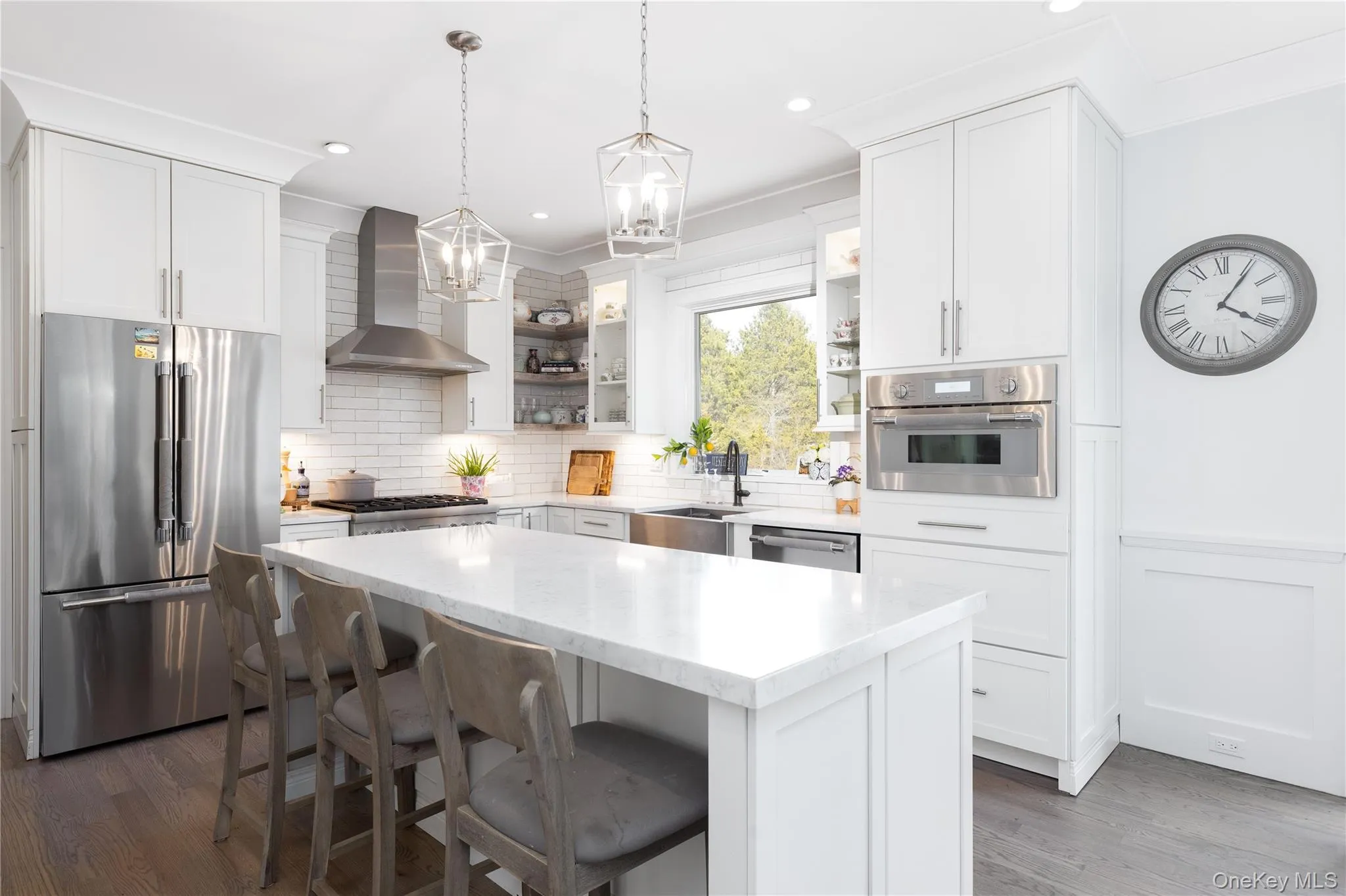 Kitchen with stainless steel appliances, a breakfast bar, pendant lighting, wall chimney range hood, and light stone countertops Kitchen with stainless steel appliances, a breakfast bar, pendant lighting, wall chimney range hood, and light stone countertops