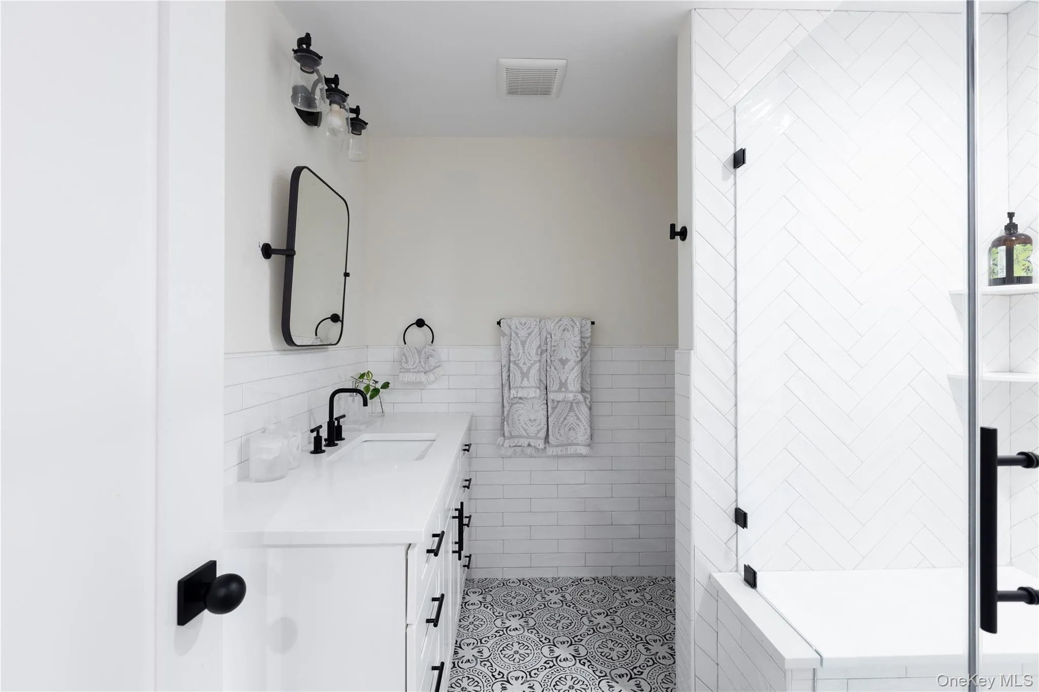 Full bathroom with tile walls, vanity, a stall shower, wainscoting, and light tile patterned floors Full bathroom with tile walls, vanity, a stall shower, wainscoting, and light tile patterned floors