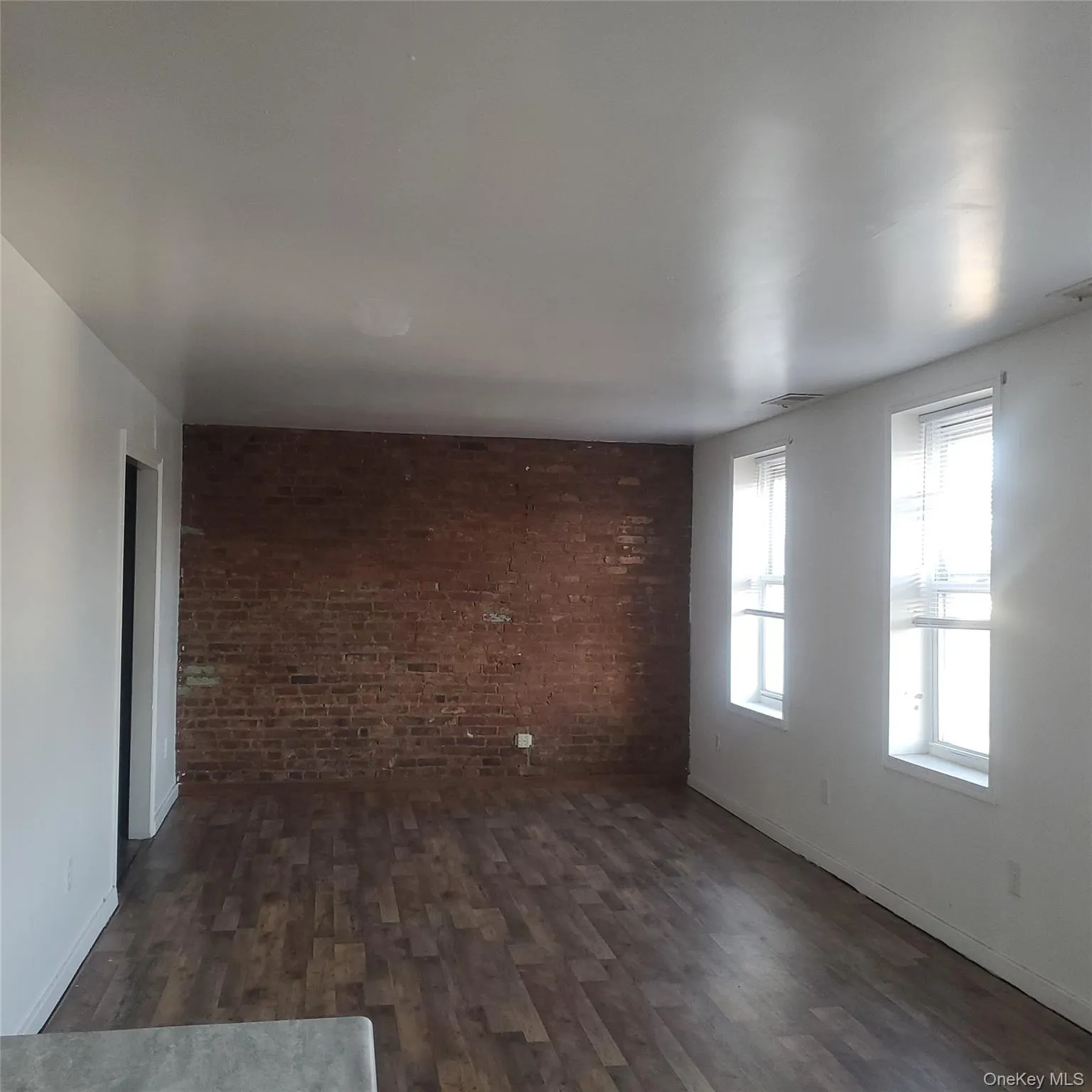 Unfurnished living room featuring brick wall and dark wood-style floors Unfurnished living room featuring brick wall and dark wood-style floors