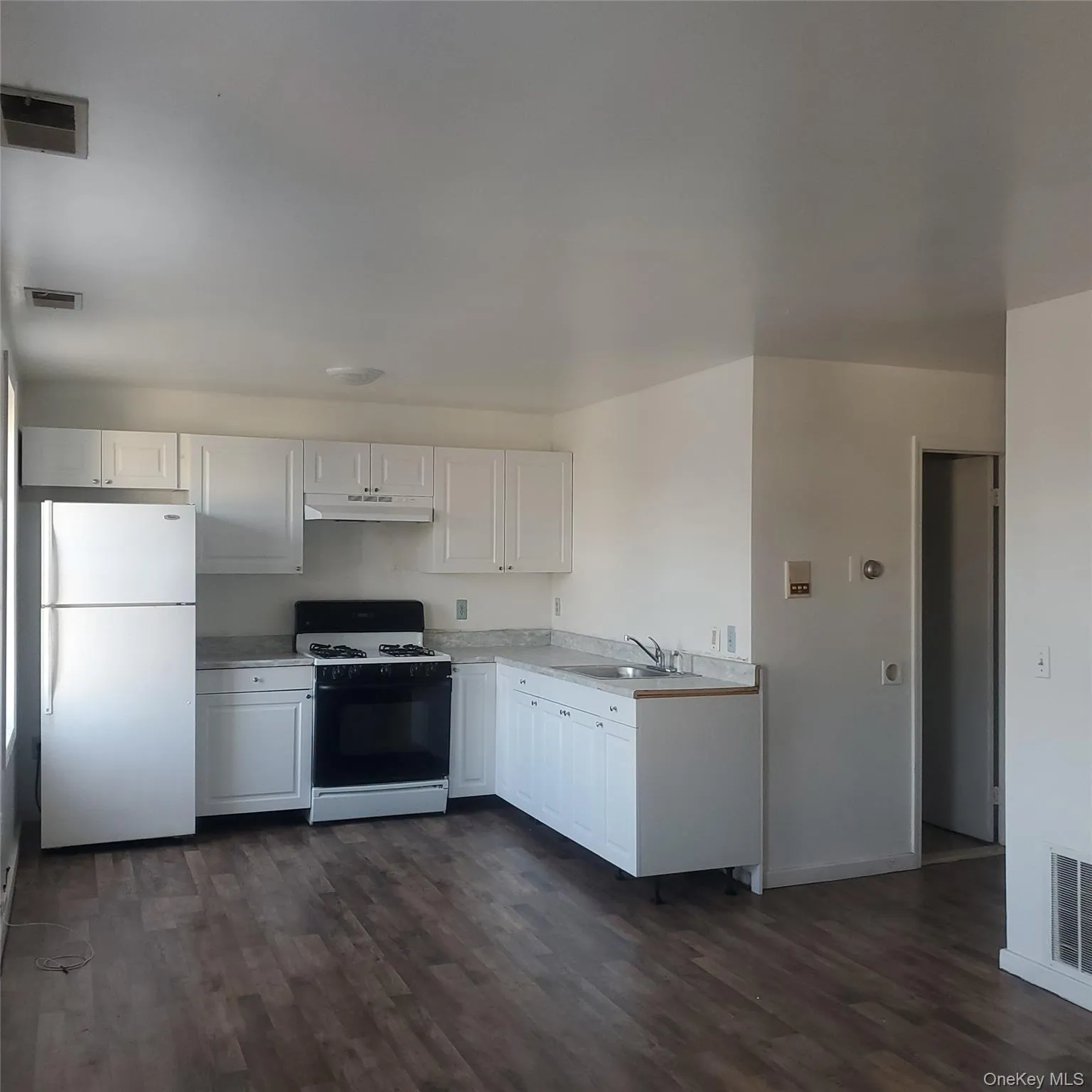 Kitchen with white cabinets, gas range, freestanding refrigerator, light countertops, and dark wood-style flooring Kitchen with white cabinets, gas range, freestanding refrigerator, light countertops, and dark wood-style flooring