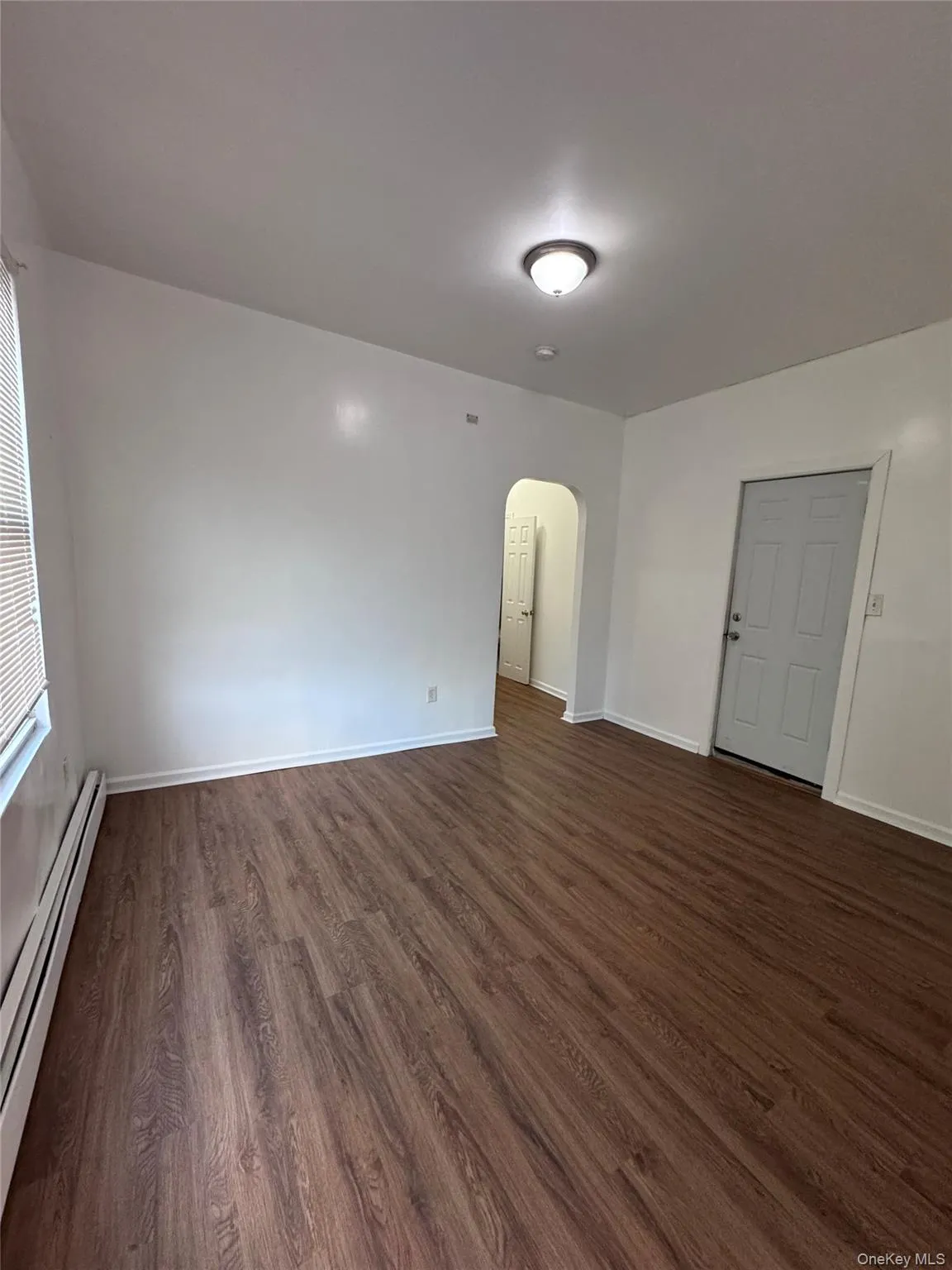 Empty room featuring arched walkways, a baseboard heating unit, and dark wood-style flooring Empty room featuring arched walkways, a baseboard heating unit, and dark wood-style flooring