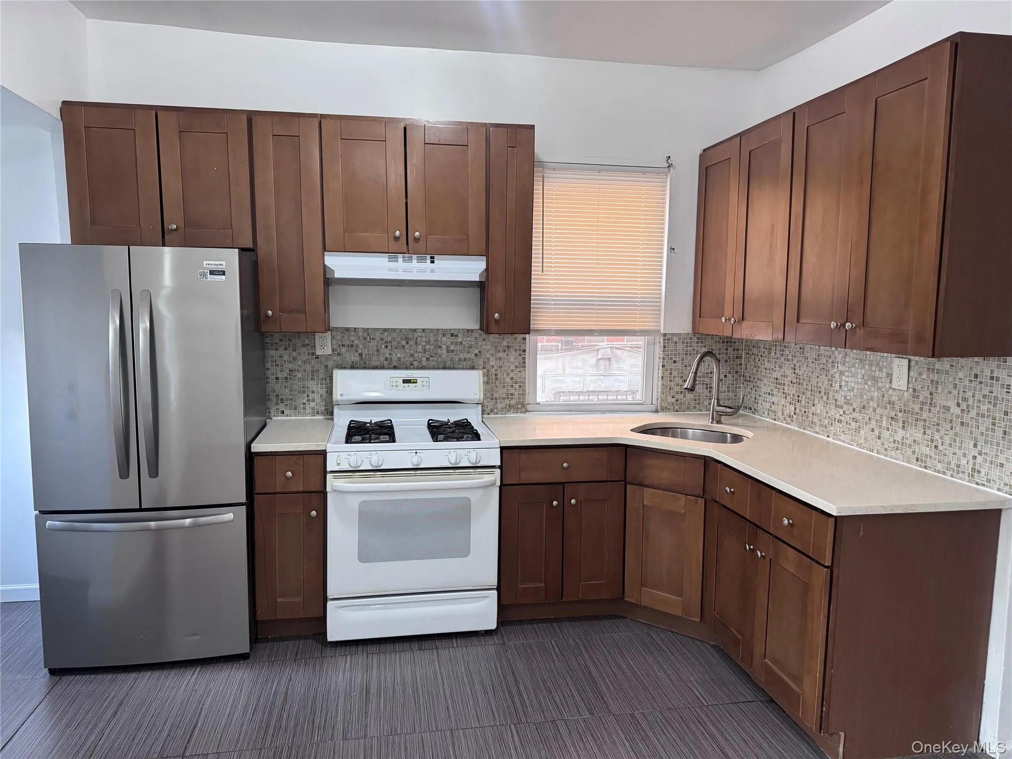 Kitchen with white range with gas cooktop, freestanding refrigerator, under cabinet range hood, light stone counters, and backsplash Kitchen with white range with gas cooktop, freestanding refrigerator, under cabinet range hood, light stone counters, and backsplash