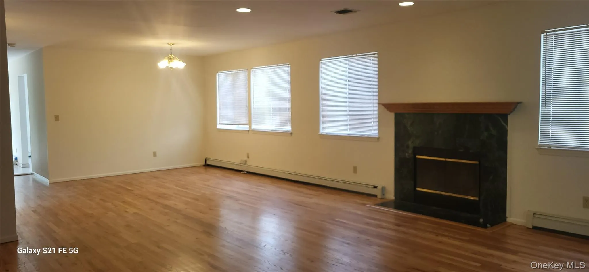 Unfurnished living room with a glass covered fireplace, a baseboard radiator, wood finished floors, recessed lighting, and a chandelier Unfurnished living room with a glass covered fireplace, a baseboard radiator, wood finished floors, recessed lighting, and a chandelier