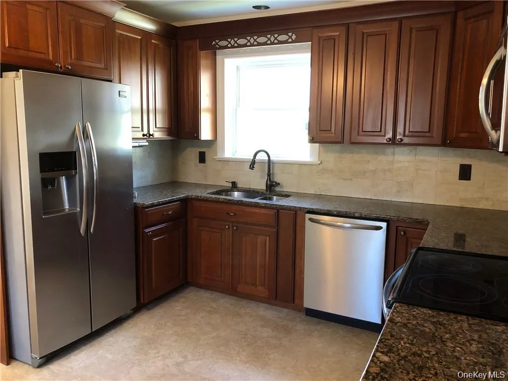 Kitchen with stainless steel appliances, dark stone counters, light flooring, and decorative backsplash Kitchen with stainless steel appliances, dark stone counters, light flooring, and decorative backsplash