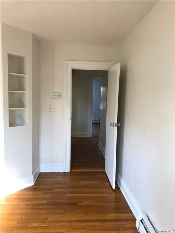 Corridor featuring dark wood finished floors, built in shelves, and baseboard heating Corridor featuring dark wood finished floors, built in shelves, and baseboard heating