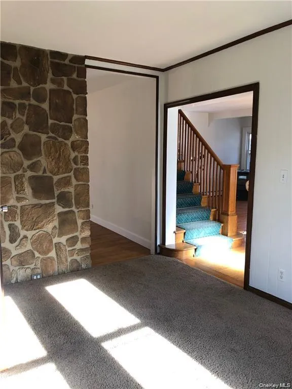 Carpeted empty room with wood finished floors, crown molding, and stairway Carpeted empty room with wood finished floors, crown molding, and stairway