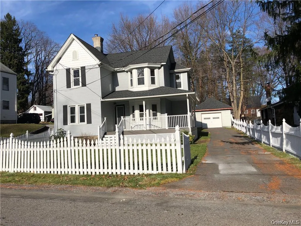 Victorian house featuring covered porch, a fenced front yard, a detached garage, a chimney, and an outdoor structure Victorian house featuring covered porch, a fenced front yard, a detached garage, a chimney, and an outdoor structure