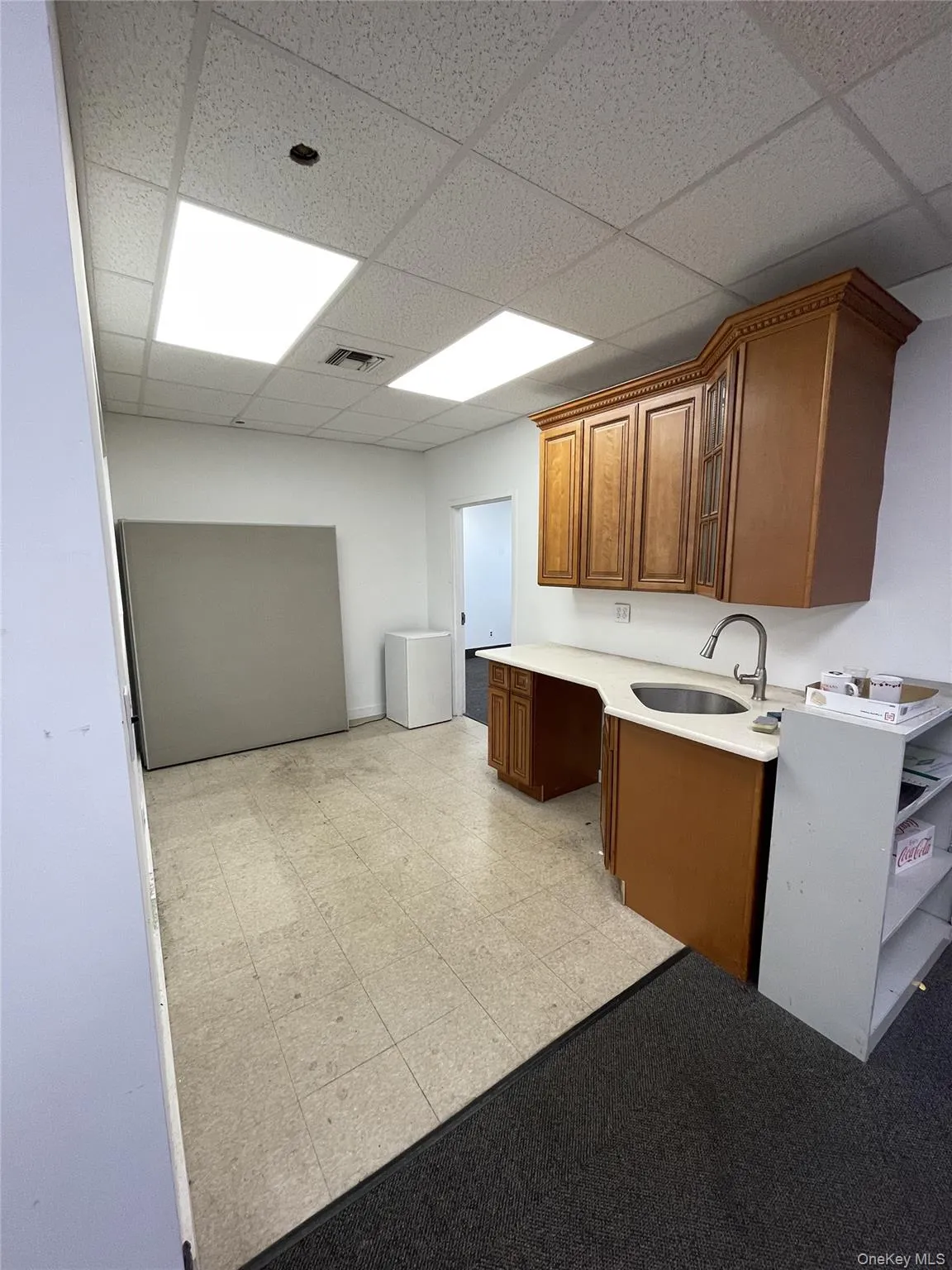 Kitchen featuring brown cabinetry, a paneled ceiling, light countertops, white fridge, and glass insert cabinets Kitchen featuring brown cabinetry, a paneled ceiling, light countertops, white fridge, and glass insert cabinets