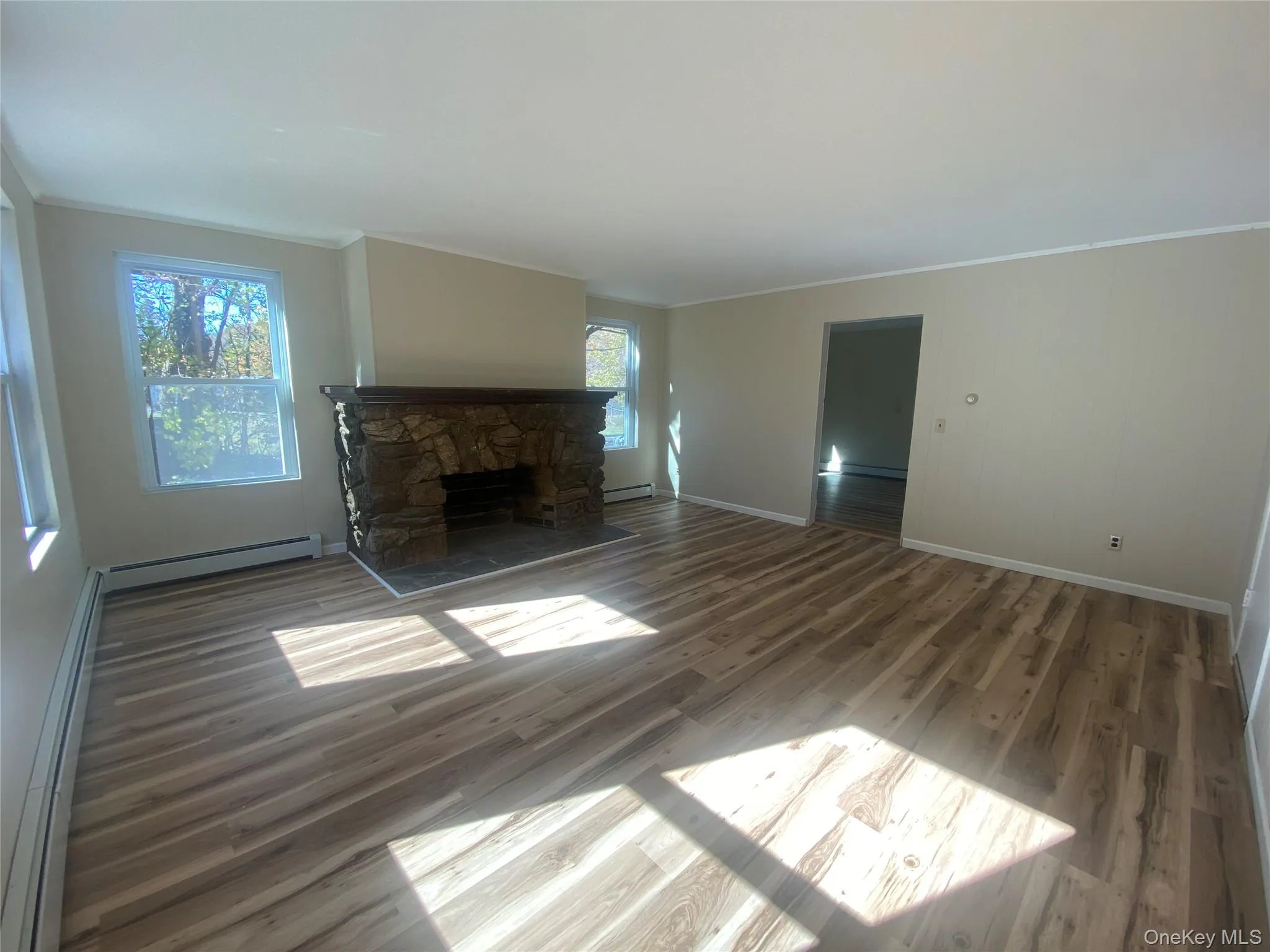 Unfurnished living room featuring a baseboard radiator, crown molding, wood finished floors, and a stone fireplace Unfurnished living room featuring a baseboard radiator, crown molding, wood finished floors, and a stone fireplace