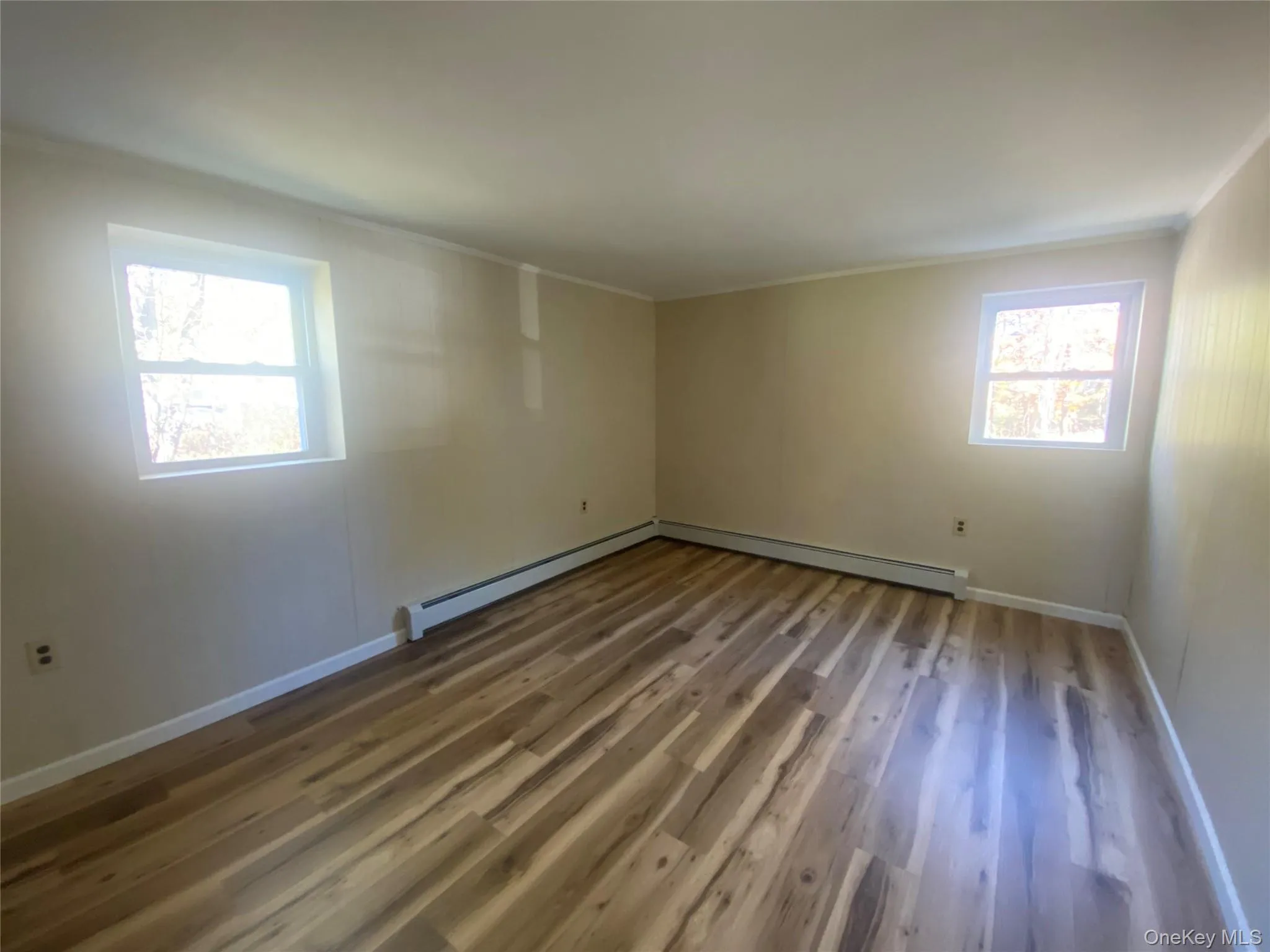 Empty room featuring wood finished floors, ornamental molding, and baseboard heating Empty room featuring wood finished floors, ornamental molding, and baseboard heating
