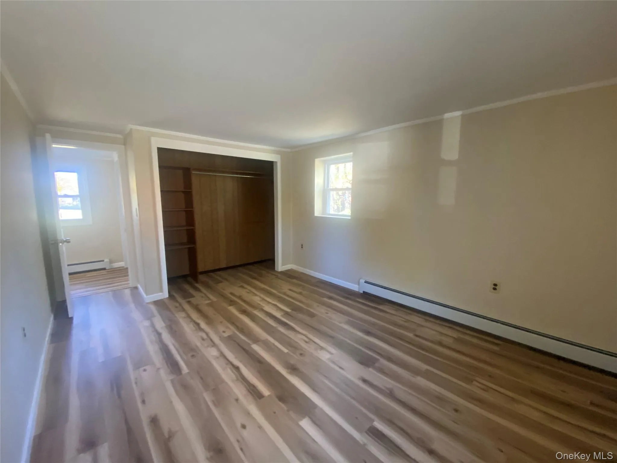 Unfurnished bedroom with dark wood-style floors, a closet, ornamental molding, and a baseboard heating unit Unfurnished bedroom with dark wood-style floors, a closet, ornamental molding, and a baseboard heating unit