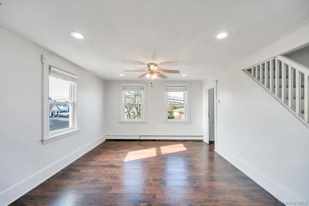 Unfurnished living room with dark wood-style floors, recessed lighting, stairway, ceiling fan, and baseboard heating Unfurnished living room with dark wood-style floors, recessed lighting, stairway, ceiling fan, and baseboard heating
