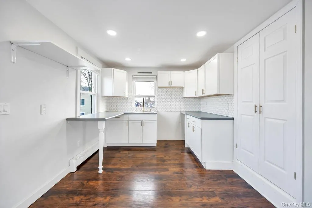 Kitchen featuring white cabinets, dark wood finished floors, backsplash, recessed lighting, and a baseboard heating unit Kitchen featuring white cabinets, dark wood finished floors, backsplash, recessed lighting, and a baseboard heating unit