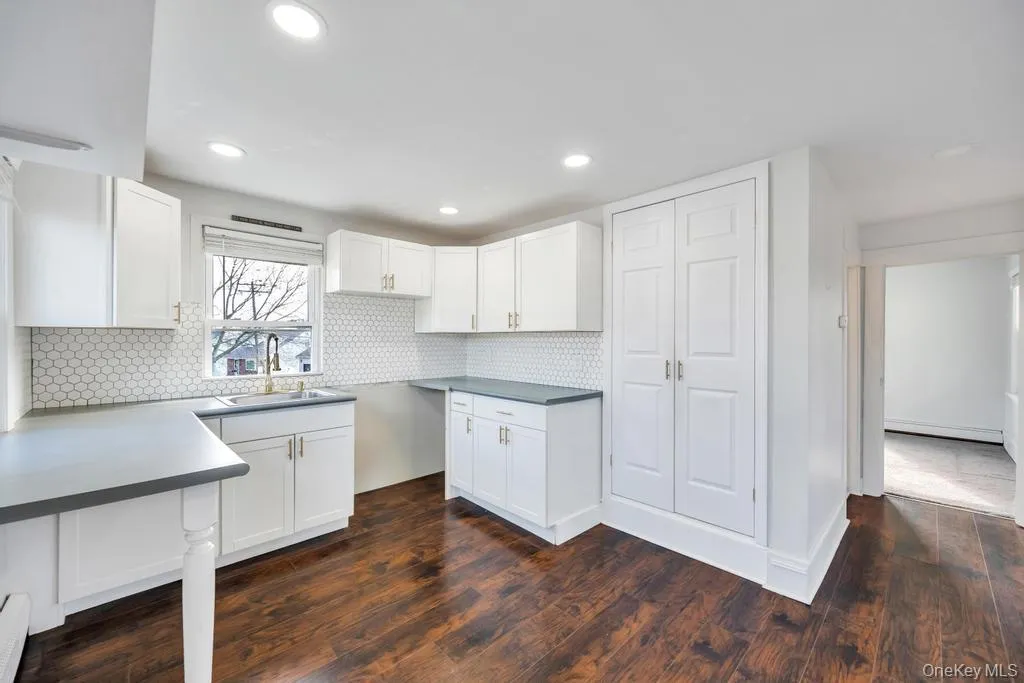Kitchen with white cabinets, backsplash, dark wood-type flooring, recessed lighting, and a baseboard radiator Kitchen with white cabinets, backsplash, dark wood-type flooring, recessed lighting, and a baseboard radiator