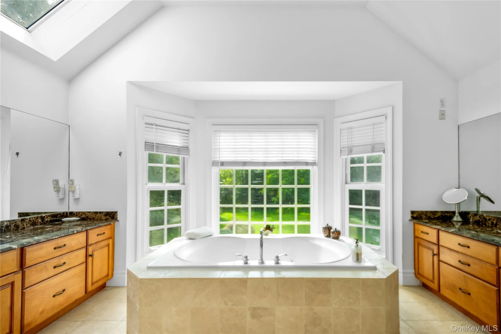 Full bathroom with a bath, a skylight, lofted ceiling, vanity, and light tile patterned floors Full bathroom with a bath, a skylight, lofted ceiling, vanity, and light tile patterned floors